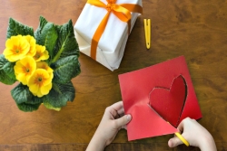 Hands of a young child using scissors to cut a heart out of red paper